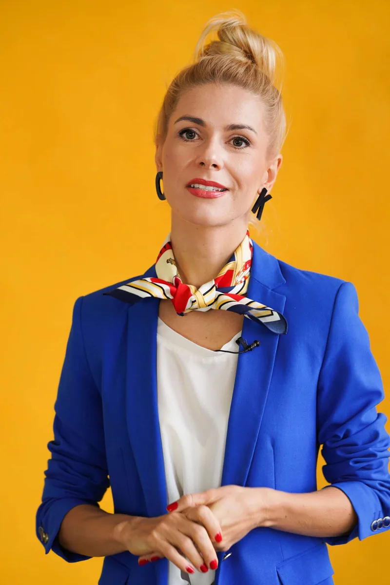 Olga Kairienė mėlynu švarku ir skarele, geltoname fone